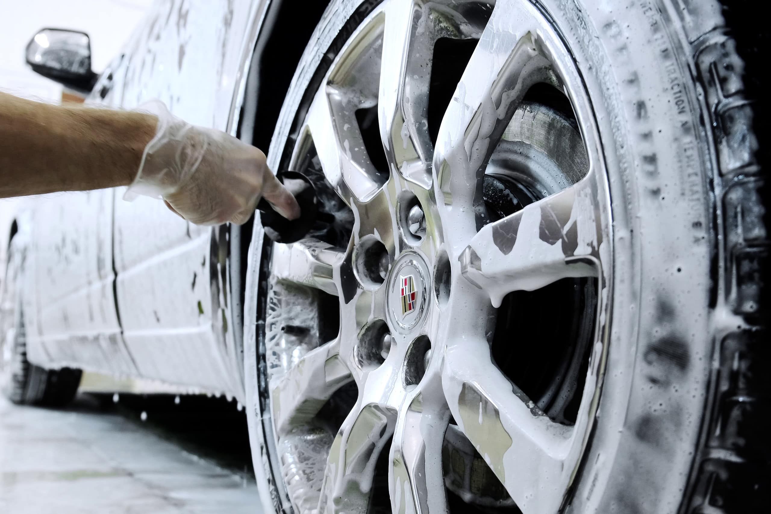 Man washes a brown Cadillac at a car wash. Close-up of washing discs by hand with a brush. Zoom out. Car detailing. Russia, Rostov-on-Don 11oct2022